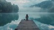 © vadosloginov - A woman sits on a dock by a lake, looking out at the water. The scene is peaceful and serene, with the misty atmosphere adding to the sense of calm. The woman is lost in thought