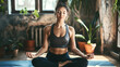 © OMD - A woman practicing yoga in a serene indoor setting, sitting in a cross-legged pose with her eyes closed, surrounded by potted plants.
