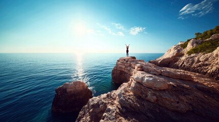 Person standing on a rocky cliff with arms raised, overlooking a calm sea under a clear sky with the sun shining brightly.