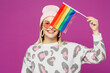 © ViDi Studio - Young lesbian woman wear pink animal clothes hold in hand cover half of face eye with striped rainbow flag isolated on plain purple background studio portrait. Pride day June month love LGBTQ concept.