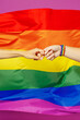 © ViDi Studio - Close up cropped photo shot of two female hands wearing bracelet holding forefinger fingers together on rainbow colorful striped flag background studio. Pride day June month love LGBTQ concept..