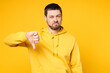 © ViDi Studio - Young dissatisfied displeased sad Caucasian man he wearing hoody casual clothes showing thumb down dislike gesture looking camera isolated on plain yellow orange background studio. Lifestyle concept.