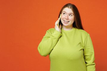 Wall Mural - Young ginger chubby plus size woman wear green sweatshirt casual clothes talk speak on mobile cell phone look aside isolated on red orange background studio portrait. Lifestyle body positive concept.