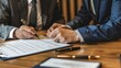 © Jayk - Two professionals in suits reviewing and signing a document at a desk, make a deal concept