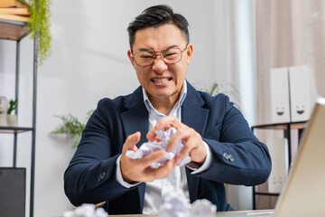 Wall Mural - Angry furious Asian businessman working at office throwing crumpled paper nervous breakdown at work, brainstorming, stress management, mental distress problems, losing temper, reaction on failure