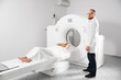 © anatoliy_gleb - Medical computed tomography or MRI scanner. Male radiologist presses MRI button to examine female patient, looking to the camera. Concept of healthcare and modern diagnostics.