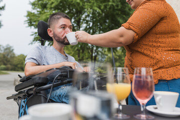 Girlfriend assisting her boyfriend with physical disability drinking coffee in a cafe. Love and conquering adversity concepts.