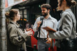 © qunica.com - Group of three businesspeople having a friendly conversation outdoors in an urban setting near a bus stop, exchanging ideas and collaborating.
