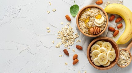 Ingredients for preparing oatmeal in a wooden bowl with almonds banana slices honey oat flakes and a spoon on a white surface Top view with space for text