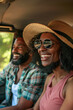 © sommersby - A smiling couple, a man and a woman, wearing sunglasses and hats, enjoys a scenic road trip together. They are seated inside a car with the window open, indicating a warm and sunny day