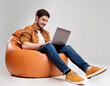 © Aleksandr Matveev - A man is sitting on a bean bag chair and using a laptop. He is smiling and he is enjoying himself. Concept of relaxation and leisure