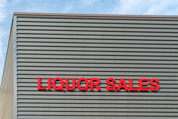 A grey exterior wall of a wholesale business with large red text letters. The liquor sales signage is displayed for the sale of beverages such as beer, wine, and spirits at an alcohol retail company.