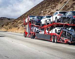 Wall Mural - Industrial big rig semi-truck car hauler transporting cars on the red semi trailer driving uphill on the mountain road