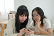 © bongkarn - Two Asian female friends are watching something on a smartphone together while sitting in a cafe.
