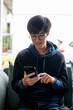 © bongkarn - A happy Asian man chatting with his friends on his smartphone while relaxing on a couch at home.