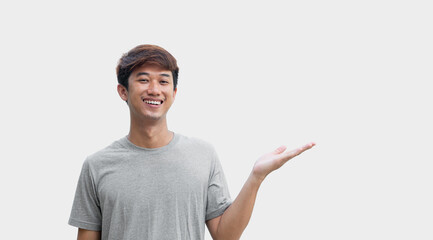 A young Asian man in his 20s wearing a gray t-shirt making a welcome gesture or presenting isolated on a gray background. Space for advertisements or welcome messages. Happy man. Positive person.