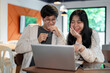 © bongkarn - Two cheerful young Asian college students are laughing at something on a laptop, enjoying talking.