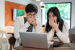 © bongkarn - Two excited Asian friends are covering their mouths and are amazed by something on a laptop screen.
