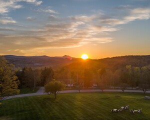 Poster - Scenic sunset over a lush green park with distant mountains and a clear sky