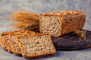 Freshly baked bread on wooden cutting board with ears of wheat.