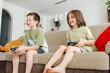 © Westend61 - Happy siblings sitting on sofa and playing video game at home