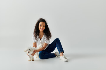 Wall Mural - A young woman sits on the floor, gently holding her small Bichon Frise dog.