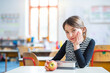 © Halfpoint - Portrait of schoolgirl, pupil sitting at desk in classroom at the elementary school. Student girl holding apple during snack time, break