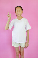 Wall Mural - Portrait of Asian girl child showing victory sign fingers isolated on pink studio background.