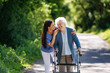 © Halfpoint - Female caregiver and senior woman with walker on walk in nature. Nurse and elderly woman enjoying a warm day in nursing home, public park.