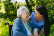 © Halfpoint - Female caregiver and senior woman in wheelchair picking wild flowers. Nurse and elderly woman enjoying a warm day in nursing home, public park.