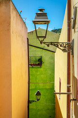 Wall Mural - Colorful yellow and green walls with a streetlamp in a street in the old mediterranean village of Bosa, Sardinia island, Italy