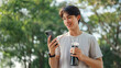 © oatawa - Happy asian man holding mobile phone and bottle of water at public park, Male using smartphone, checking mobile fitness application, copy space.