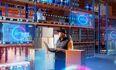 Man in innovation warehouse. Monitor storage fullness via laptop. Supervisor with computer stands in warehouse. Man near storage shelving with boxes. Supervisor conducts audit of warehouse