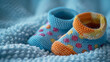 © SashaMagic - Colorful knitted baby booties on a soft blue blanket.