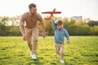 © standret - Toy plane in hand, running. Happy father with son are having fun on the field at summertime