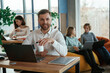© standret - Man is smiling, sitting by the table with laptop. People are working in the office with bean bags chairs in it