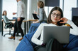 © standret - Smart woman is sitting and uses laptop. People are working in the office with bean bags chairs in it