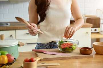 An attractive Asian woman is in the kitchen, holding a bowl of salad and a wooden spatula, enjoying cooking in the kitchen. home cooking and healthy eating life concepts