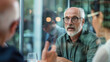 © VK Studio - An elderly gentleman with glasses engaged in a thoughtful conversation at a modern, glass-walled office.