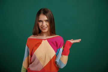 Wall Mural - Showing by hand to the side, place for text. Young woman is standing against green background in the studio