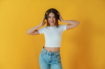 Wall Mural - In headphones, enjoying music. Young woman is against yellow background