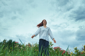 Teenage girl standing in flower field with cloudy sky background. Low angle photography