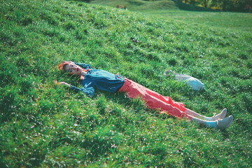 Teenage girl lying on green grass in a park with a bag nearby. Outdoor photography in a park setting. Relaxation and nature concept.