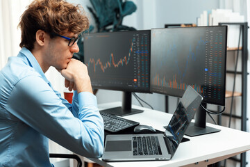 Wall Mural - Working young business trader typing, focusing on laptop in market stock graph data investment in real time laptop in screens. at modern office, analyzing dynamic financial exchange rate. Gusher.
