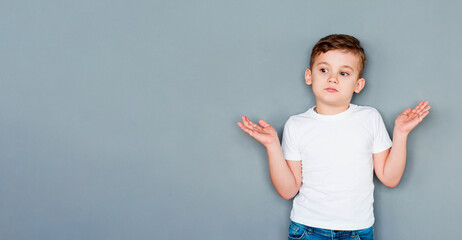 Wall Mural - Little cute boy kid wearing casual white t-shirt clueless and confused expression with arms and hands raised. doubt concept.