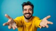 © CYBERUSS - Cheerful young man with open arms and welcoming expression on blue background