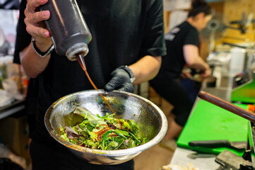 Wall Mural - A chef in a commercial kitchen pours sauce onto a fresh salad.