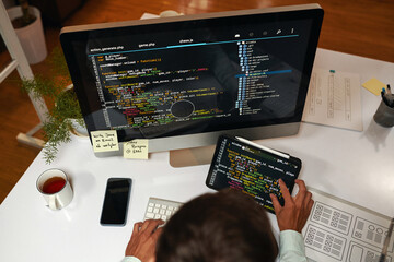 it specialist reviewing programming code on laptop and tablet computer