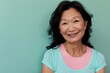 © CogniLens - Portrait of a satisfied asian woman in her 50s smiling at the camera while standing against pastel green background