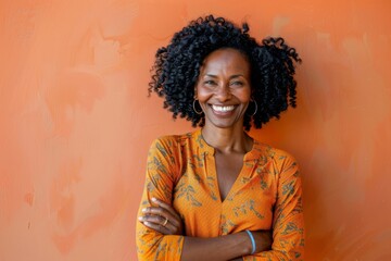 Wall Mural - Portrait of a smiling afro-american woman in her 30s with arms crossed in pastel orange background